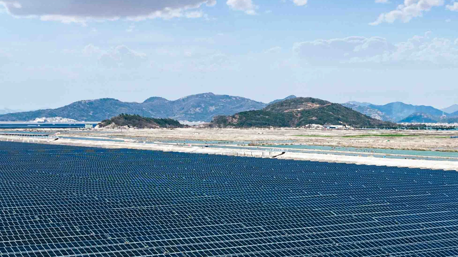Bulutlu gökyüzü altında tepelere doğru uzanan büyük bir güneş enerjisi santralinde sıra sıra güneş panelleri
